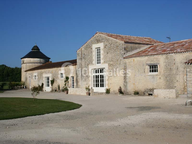 Location salle Benon (Charente-Maritime) - Abbaye de la Grâce-Dieu #2 Bâtiment en pierre avec toit en tuiles, entouré de végétation, sous un ciel bleu clair.