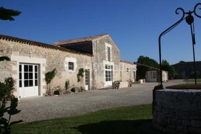 Miniature Location salle Benon (Charente-Maritime) - Abbaye de la Grâce-Dieu #3 Salon lumineux avec murs blancs, plafond voûté, cheminée centrale, meubles anciens et canapés gris.