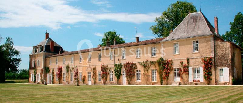 Location salle Benon (Charente-Maritime) - Abbaye de la Grâce-Dieu #7 Façade d'un grand bâtiment ancien en pierre, entouré de pelouse et de végétation grimpante, sous un ciel clair.