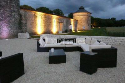 Miniature Location salle Benon (Charente-Maritime) - Abbaye de la Grâce-Dieu #6 Salon lumineux avec murs blancs, plafond voûté, cheminée centrale, meubles anciens et canapés gris.