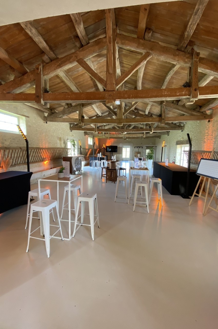 Location salle Benon (Charente-Maritime) - Abbaye de la Grâce-Dieu #9 Grande salle avec charpente en bois apparente, tables hautes blanches et décoration lumineuse chaleureuse.