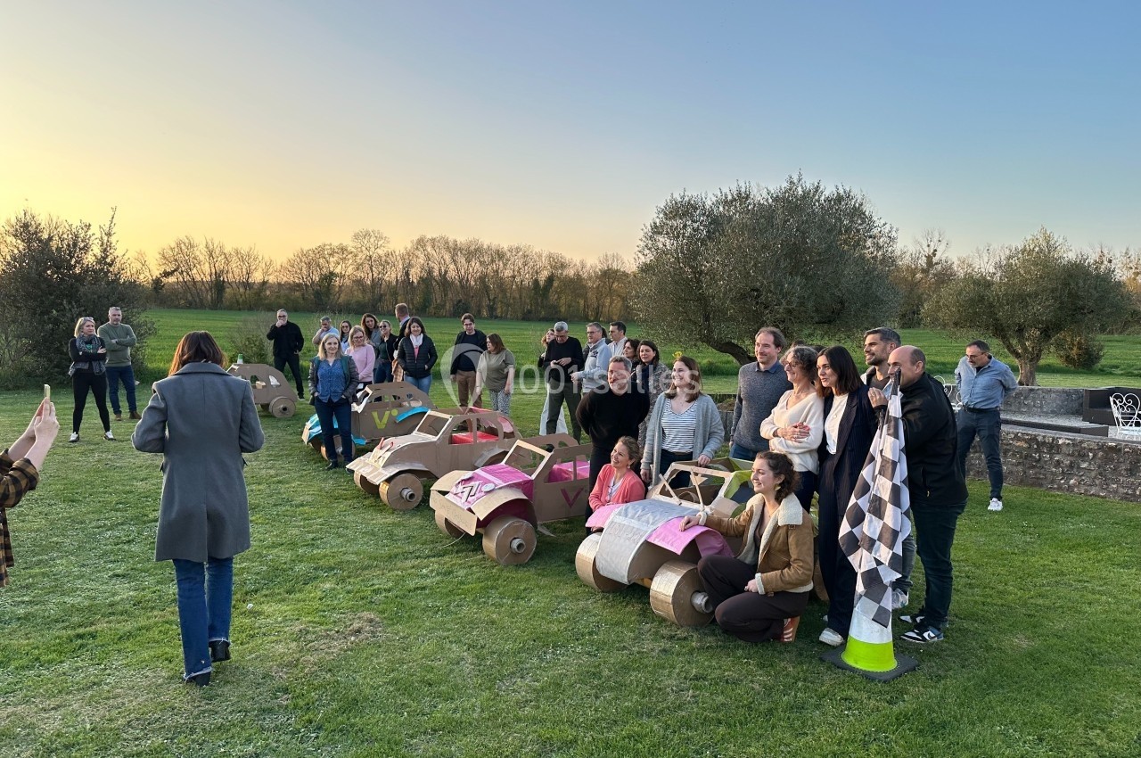 Location salle Benon (Charente-Maritime) - Abbaye de la Grâce-Dieu #5 Un groupe de personnes posant avec des voitures en carton sur une pelouse au coucher du soleil.