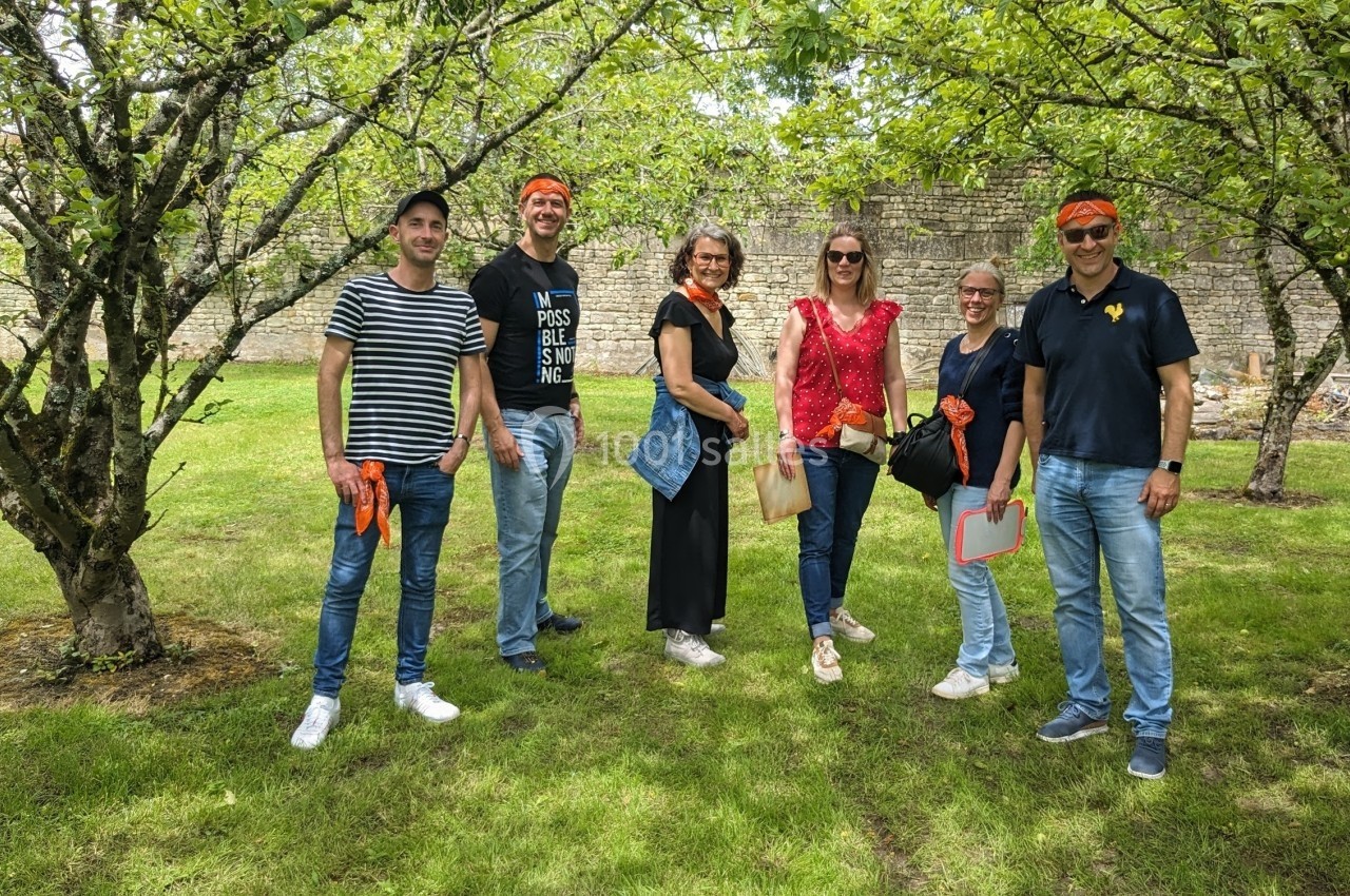 Location salle Benon (Charente-Maritime) - Abbaye de la Grâce-Dieu #10 Un groupe de six personnes posant dans un jardin verdoyant avec des arbres et un mur en pierre en arrière-plan.