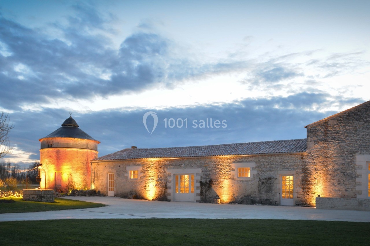 Location salle Benon (Charente-Maritime) - Abbaye de la Grâce-Dieu #15 Bâtisse en pierre éclairée au crépuscule avec une tour ronde et un ciel nuageux en arrière-plan.