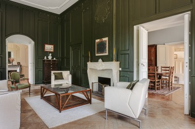 Miniature Location salle Benon (Charente-Maritime) - Abbaye de la Grâce-Dieu #17 Salon lumineux avec murs blancs, plafond voûté, cheminée centrale, meubles anciens et canapés gris.