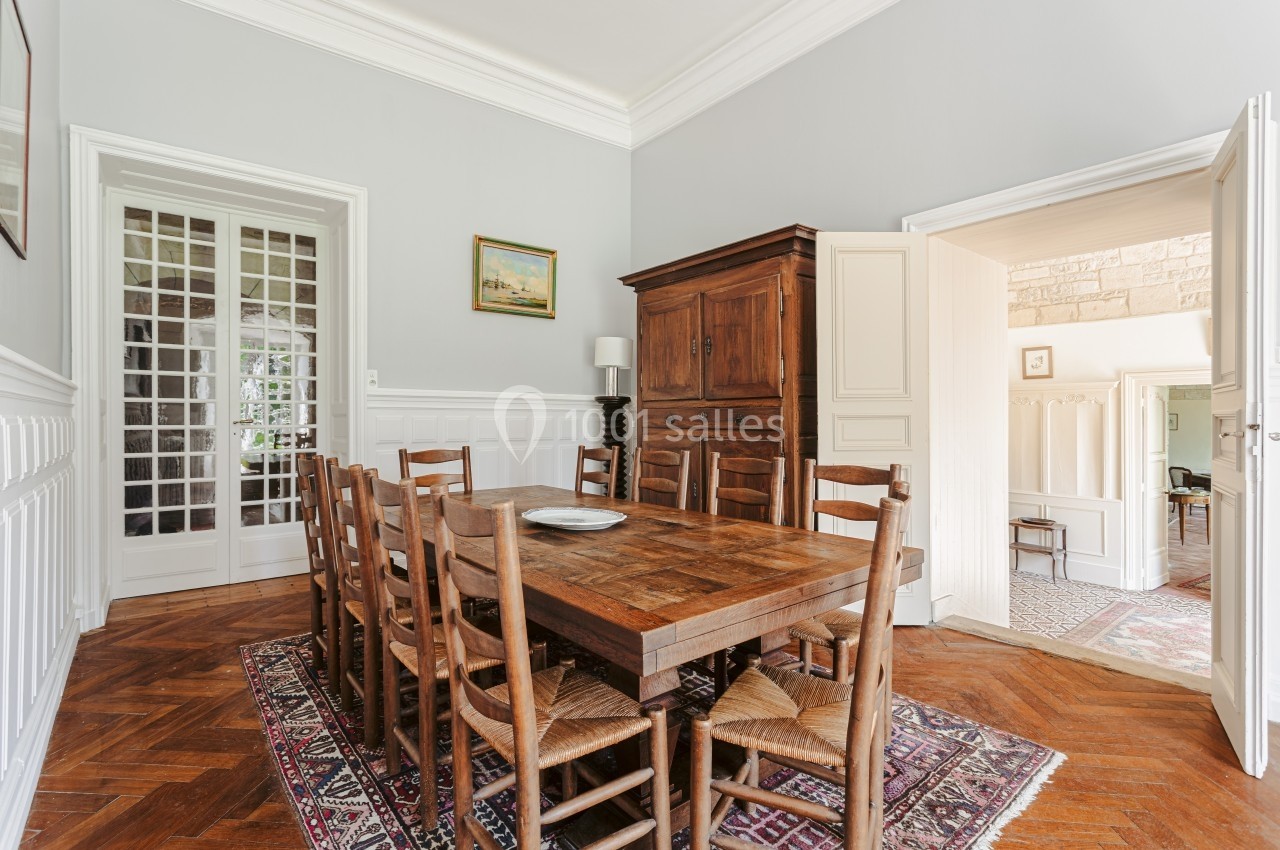 Location salle Benon (Charente-Maritime) - Abbaye de la Grâce-Dieu #18 Salle à manger lumineuse avec table en bois, chaises en paille, armoire ancienne et parquet en chevrons.