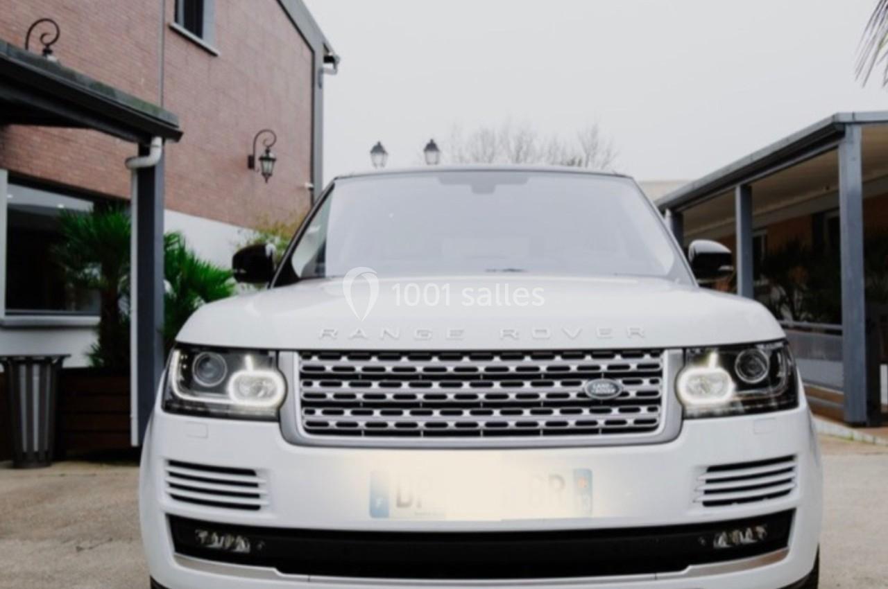 Voiture Range Rover blanche garée devant une maison en briques avec un porche et des plantes.