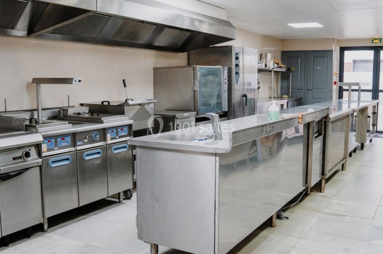 Cuisine professionnelle équipée avec plans de travail en inox, appareils de cuisson et hotte d'extraction.