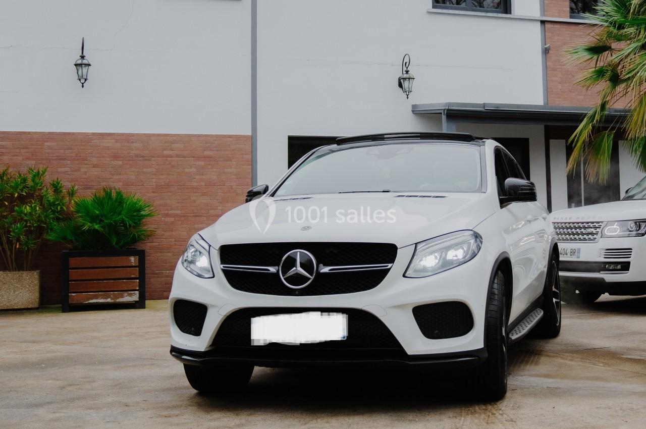 SUV blanc garé devant une maison moderne avec des murs en briques et des plantes décoratives.