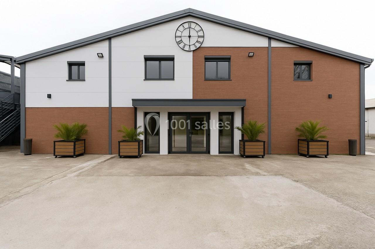 Façade d'un bâtiment moderne à deux tons avec une horloge centrale et des plantes en bacs devant l'entrée.