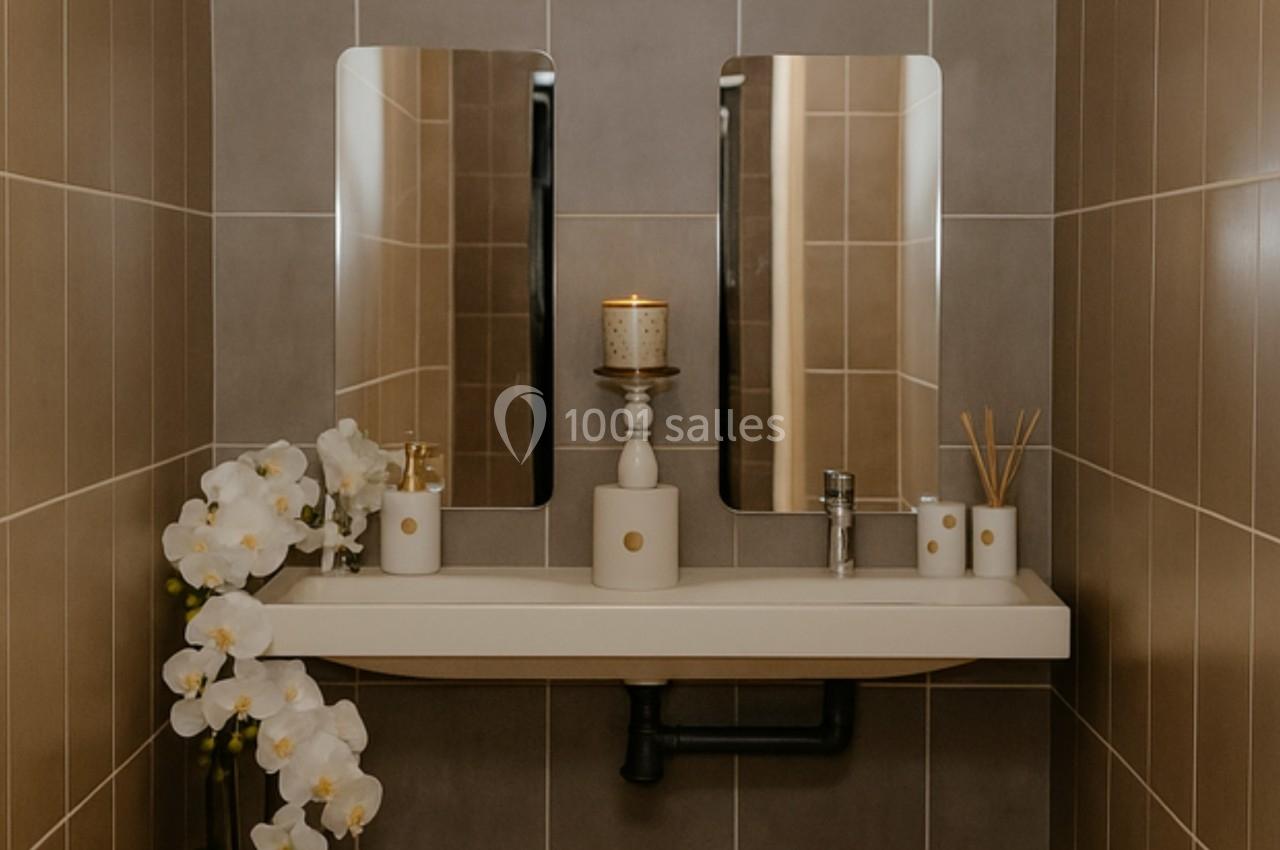 Lavabo moderne avec deux miroirs, une orchidée blanche en pot, bougie allumée et accessoires de salle de bain.