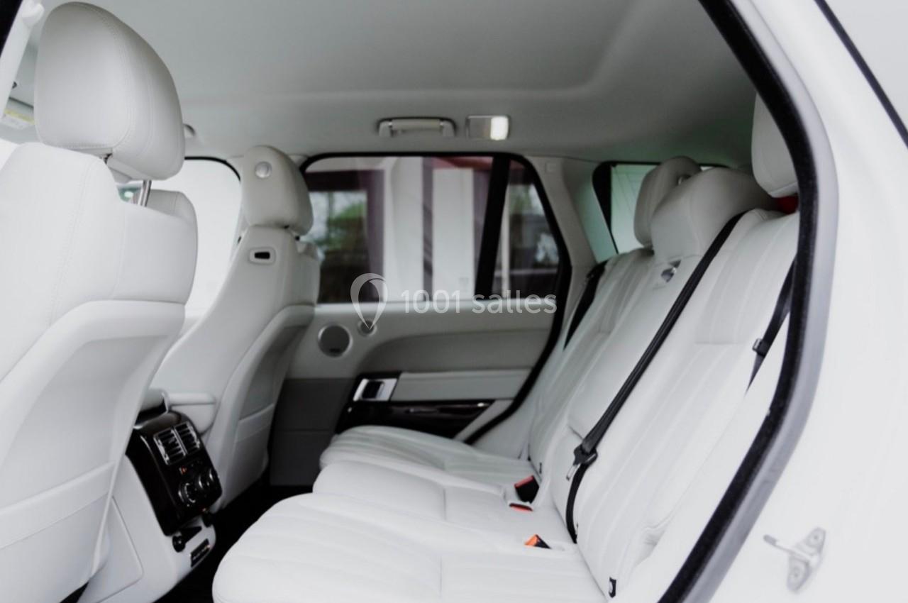 Intérieur d'une voiture avec des sièges arrière en cuir blanc, vue depuis une porte ouverte.