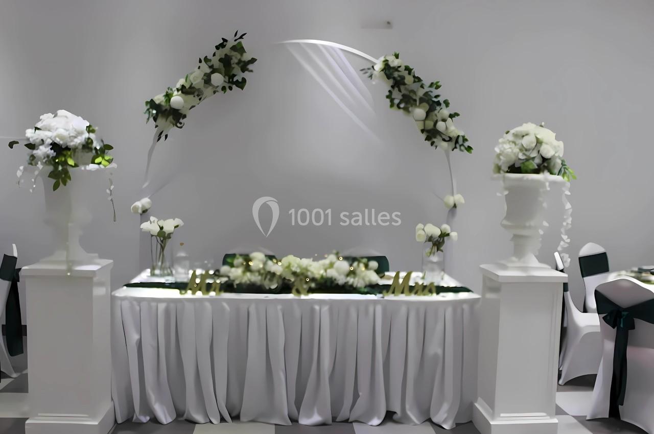 Table décorée pour un mariage avec des fleurs blanches, un arche floral et des chaises habillées de housses.