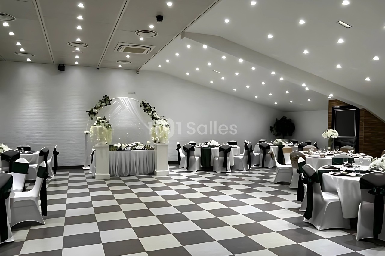 Salle de réception élégante avec tables rondes décorées de nappes blanches et un arche floral au centre.