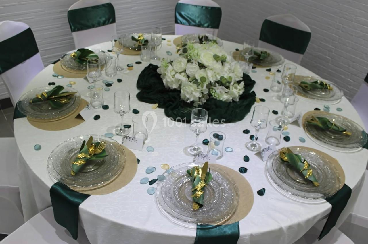 Table ronde élégamment dressée avec nappes blanches, serviettes vertes, vaisselle transparente et centre de table floral.