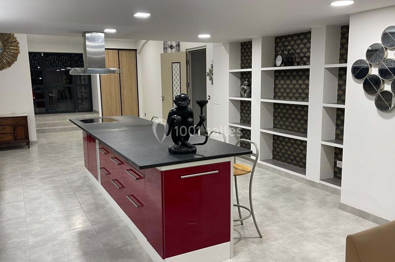 Cuisine moderne avec un îlot central rouge, plan de travail noir, étagères murales et décoration contemporaine.