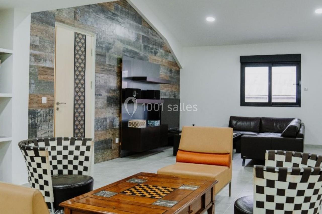 Salon moderne avec mobilier varié, murs texturés, table basse en bois et lumière naturelle provenant d'une fenêtre.