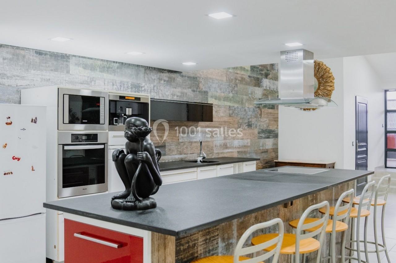 Cuisine moderne avec un îlot central, tabourets en bois, électroménagers encastrés et une statue décorative noire.