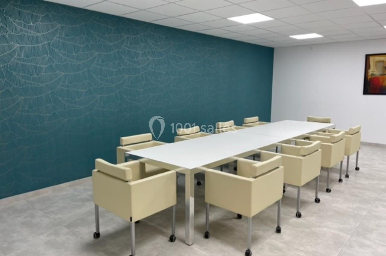 Salle de réunion moderne avec une grande table blanche, des chaises beige à roulettes et un mur bleu décoratif.