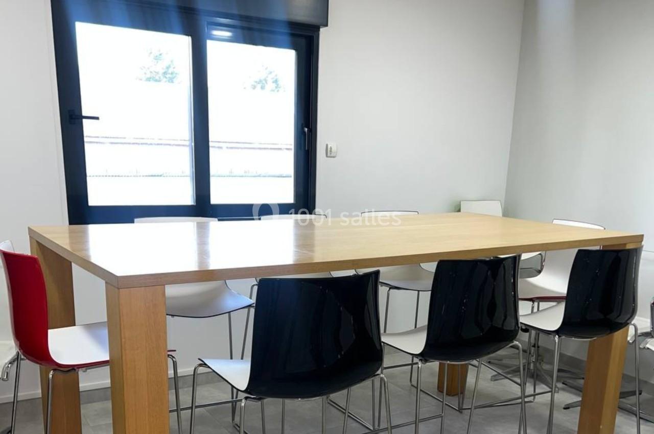 Table haute en bois entourée de chaises modernes blanches et noires dans une pièce lumineuse avec fenêtre.