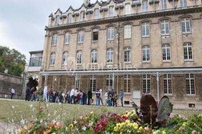 Salle lumineuse avec de grandes fenêtres, tables en bois clair et chaises alignées dans un espace de restauration collectif.
