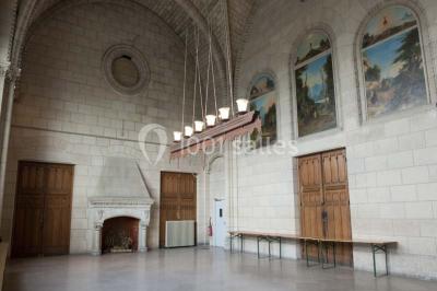 Salle lumineuse avec de grandes fenêtres, tables en bois clair et chaises alignées dans un espace de restauration collectif.