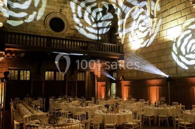 Salle lumineuse avec de grandes fenêtres, tables en bois clair et chaises alignées dans un espace de restauration collectif.
