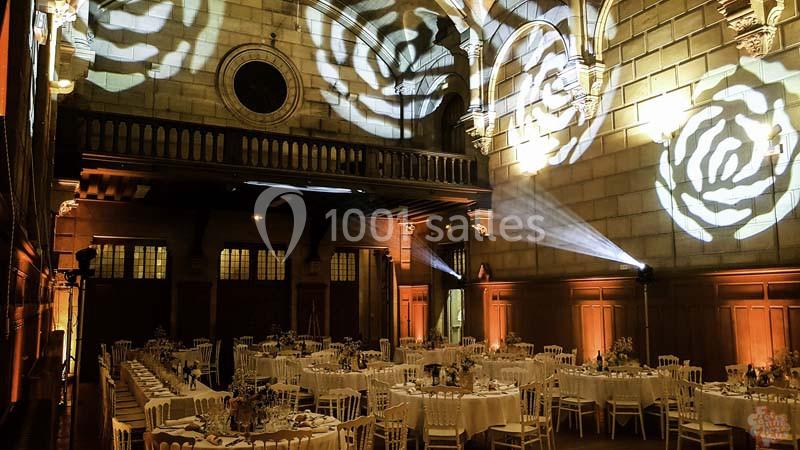 Salle de réception élégante avec tables dressées, éclairages décoratifs en forme de roses projetés sur les murs.