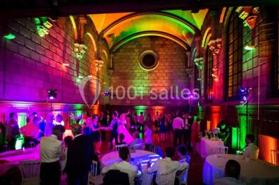 Salle lumineuse avec de grandes fenêtres, tables en bois clair et chaises alignées dans un espace de restauration collectif.