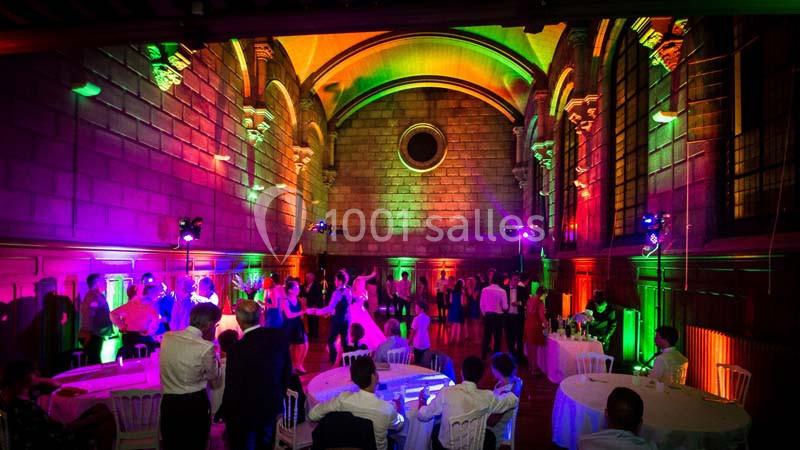 Salle voûtée éclairée de lumières colorées, avec des invités assis et d'autres dansant lors d'un événement festif.