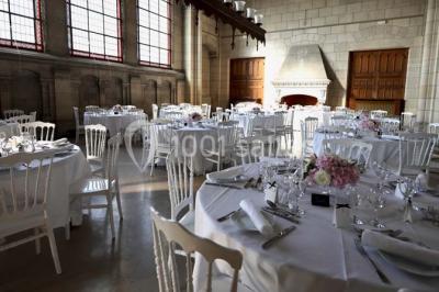 Salle lumineuse avec de grandes fenêtres, tables en bois clair et chaises alignées dans un espace de restauration collectif.