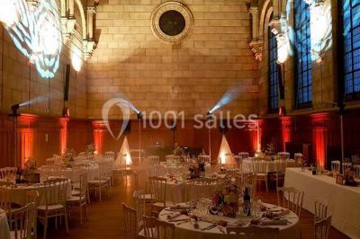 Salle lumineuse avec de grandes fenêtres, tables en bois clair et chaises alignées dans un espace de restauration collectif.