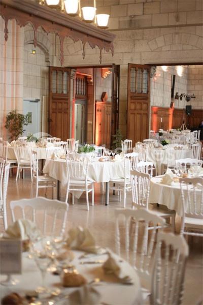 Salle de réception élégante avec des tables rondes dressées, chaises blanches et décorations sobres.