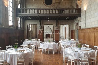 Salle lumineuse avec de grandes fenêtres, tables en bois clair et chaises alignées dans un espace de restauration collectif.