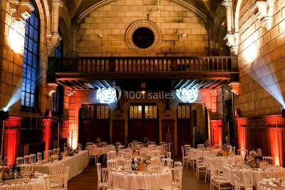Salle lumineuse avec de grandes fenêtres, tables en bois clair et chaises alignées dans un espace de restauration collectif.