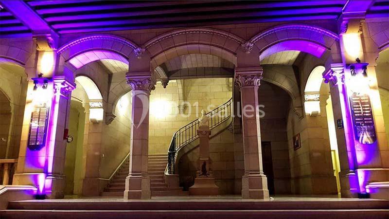 Escalier en pierre dans un bâtiment ancien, éclairé par des lumières violettes mettant en valeur les arches.