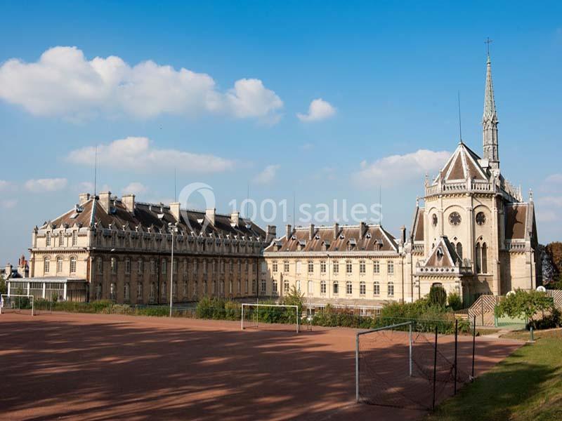 Bâtiment historique avec une chapelle et un terrain de sport au premier plan, sous un ciel partiellement nuageux.