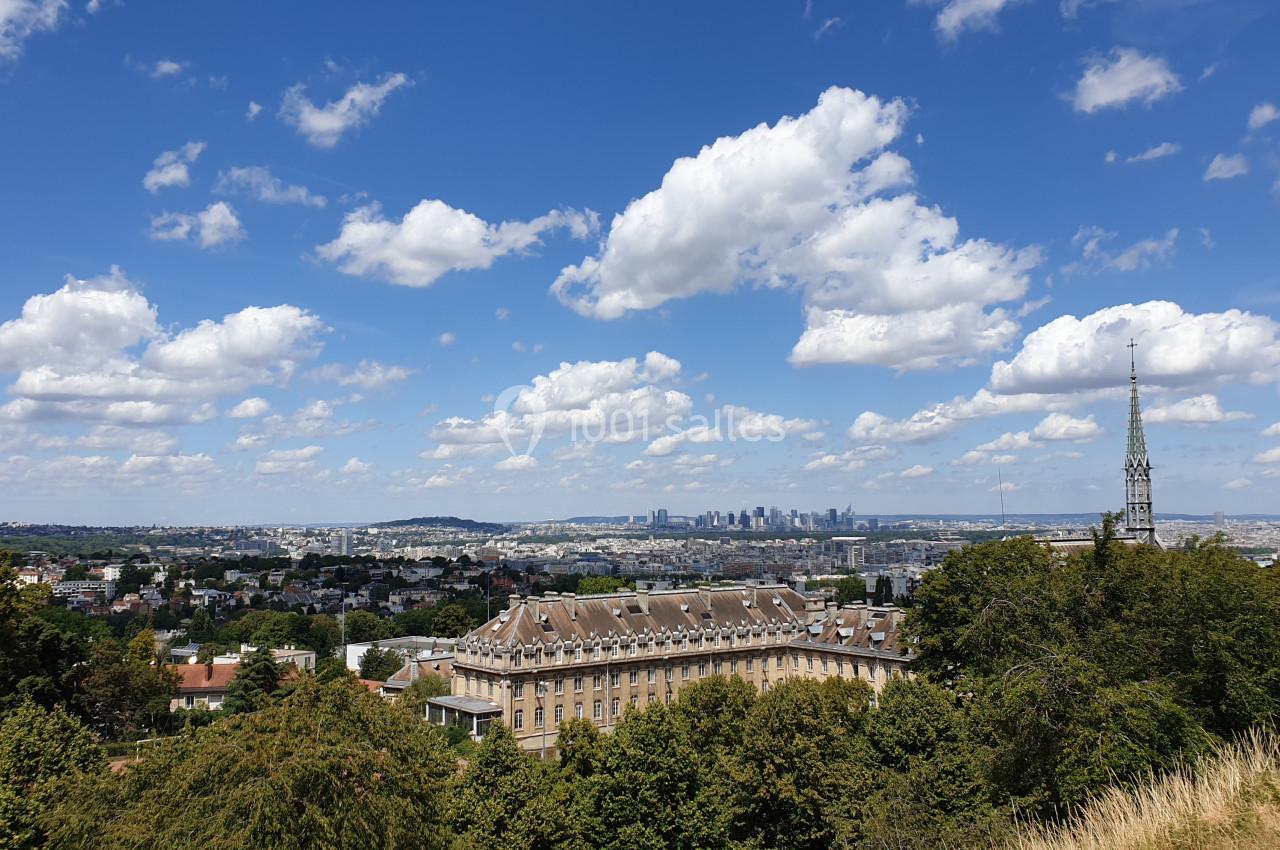 Vue panoramique sur un bâtiment historique entouré de verdure, avec la ville et des gratte-ciels à l'horizon sous un ciel…