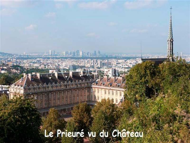 Vue d'un bâtiment historique entouré de végétation avec une ville et des gratte-ciels en arrière-plan.