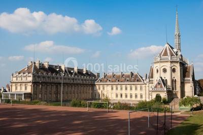 Bâtiment historique avec une chapelle et un terrain de sport au premier plan, sous un ciel partiellement nuageux.