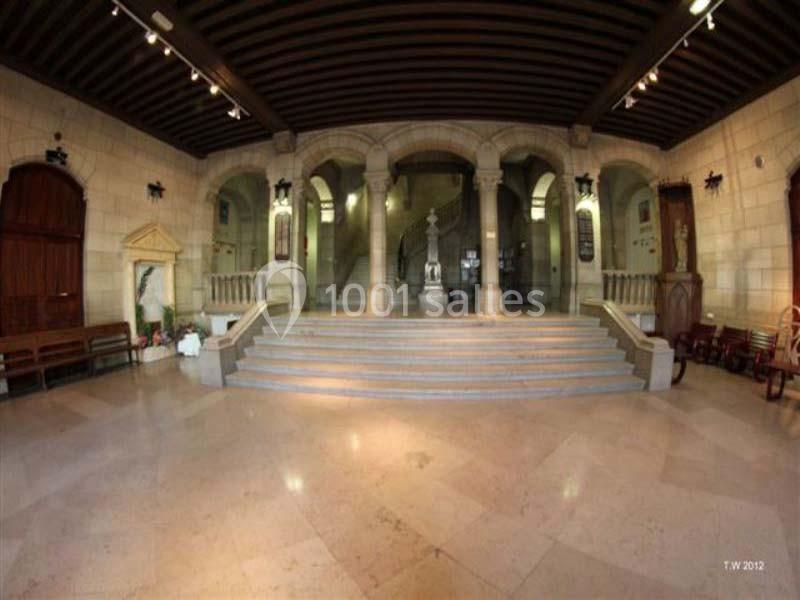 Intérieur d'un bâtiment avec des colonnes, des escaliers centraux et une statue au fond sous un éclairage tamisé.