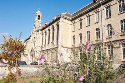 Bâtiment historique avec une chapelle et un terrain de sport au premier plan, sous un ciel partiellement nuageux.