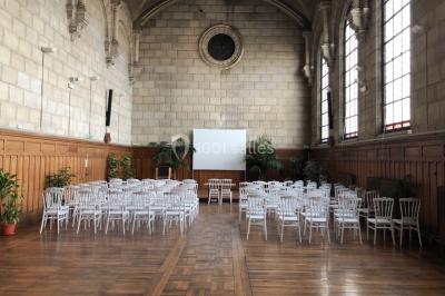 Bâtiment historique avec une chapelle et un terrain de sport au premier plan, sous un ciel partiellement nuageux.