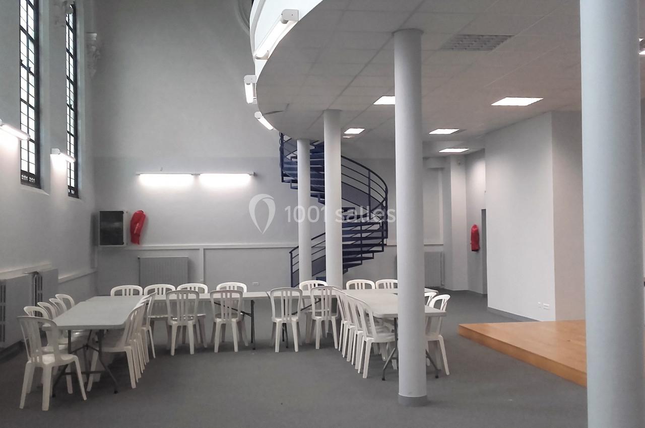 Salle lumineuse avec tables et chaises blanches, escalier en colimaçon bleu et murs clairs.