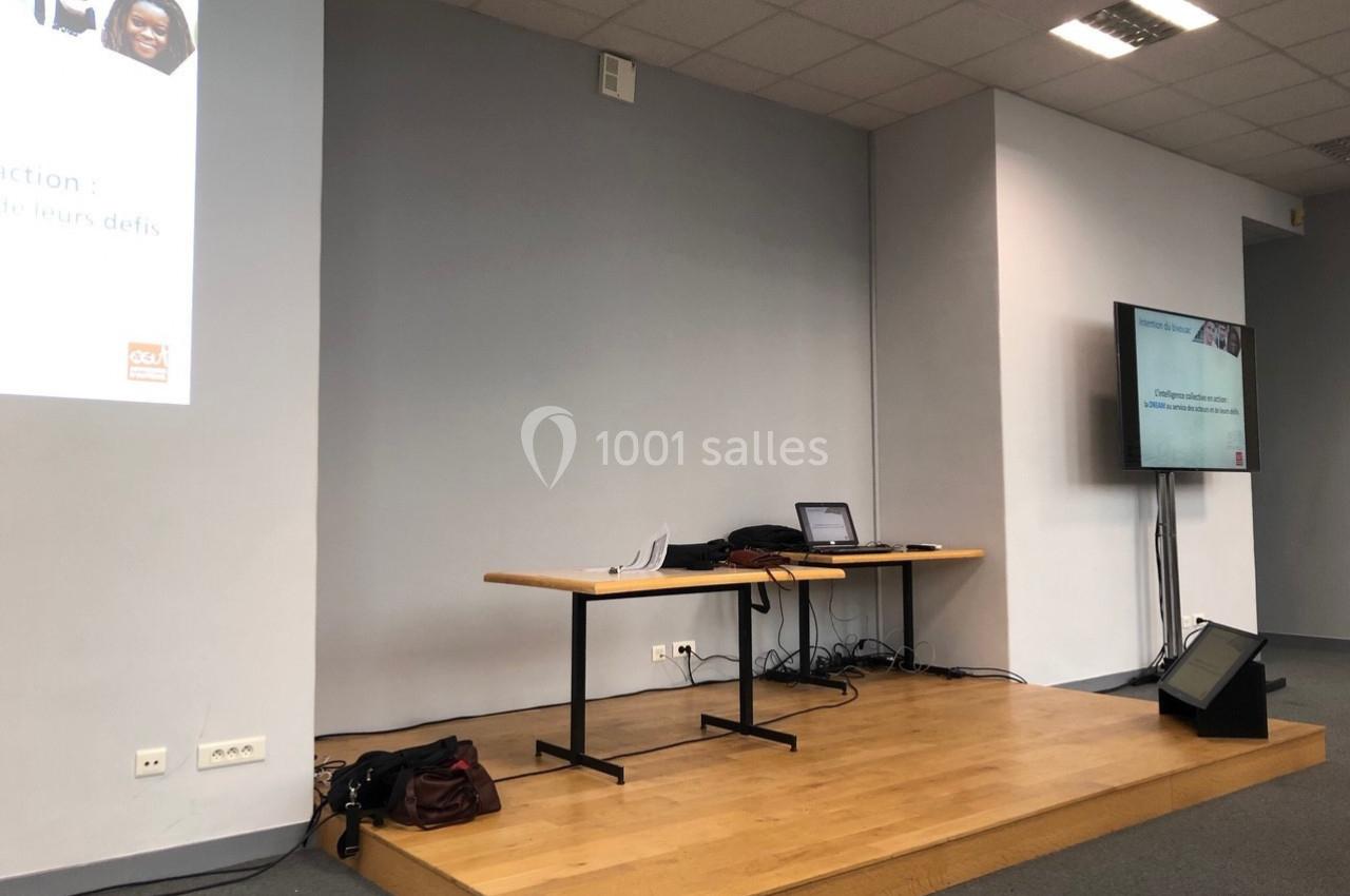 Salle de conférence avec une estrade, un écran de projection, un ordinateur portable et un écran secondaire.