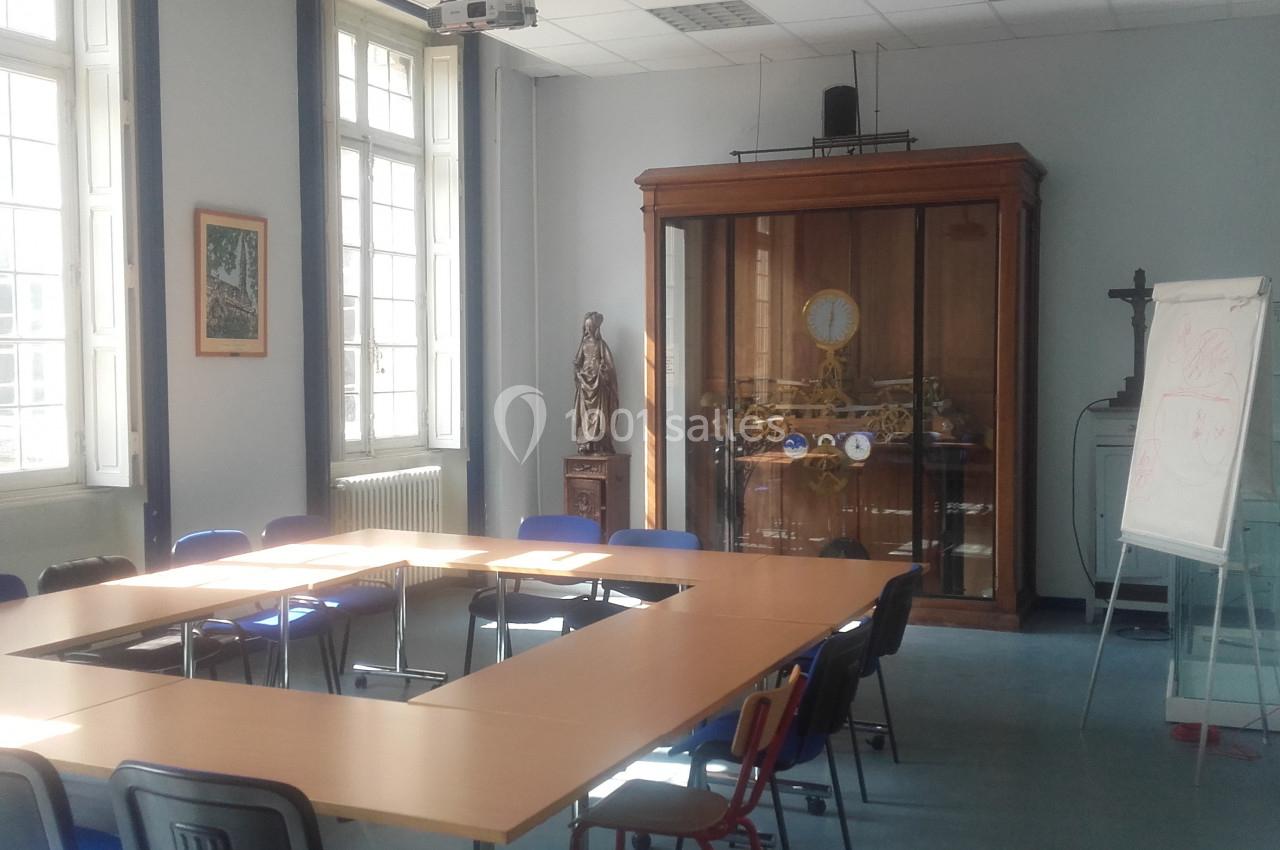 Salle de réunion lumineuse avec une table en U, des chaises, un tableau blanc et une grande vitrine en bois.