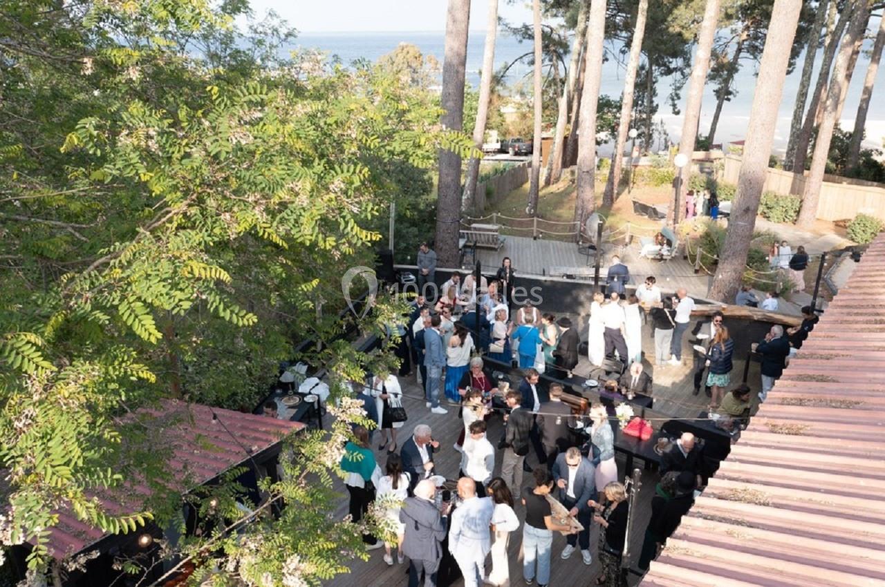 Groupe de personnes rassemblées en extérieur dans un espace boisé près de la mer, sous une lumière naturelle.