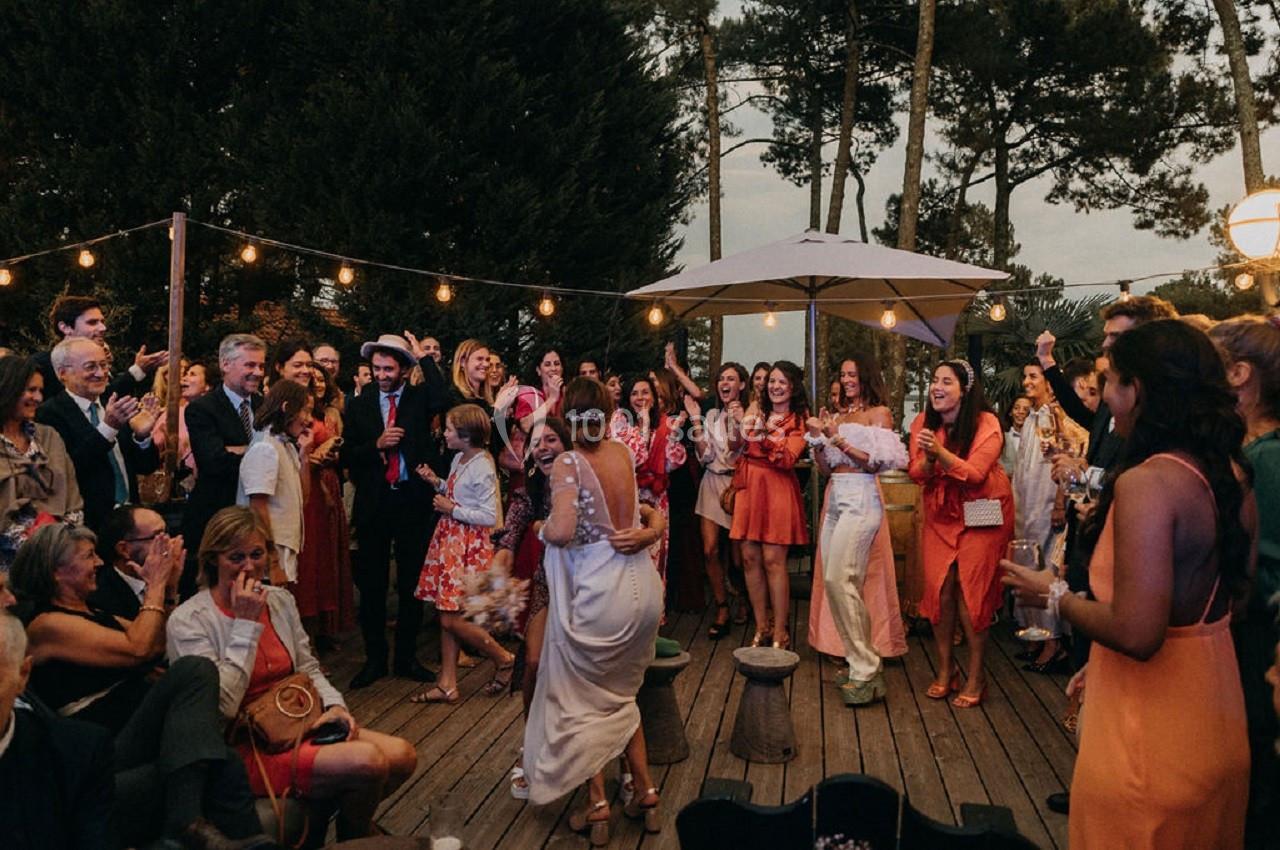 Groupe de personnes célébrant en extérieur sur une terrasse en bois, entourées de guirlandes lumineuses et d'arbres.