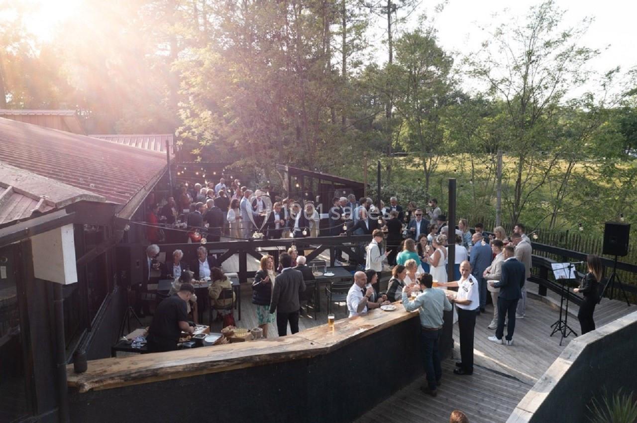 Groupe de personnes réunies en extérieur sur une terrasse en bois, entourée d'arbres, lors d'un événement.