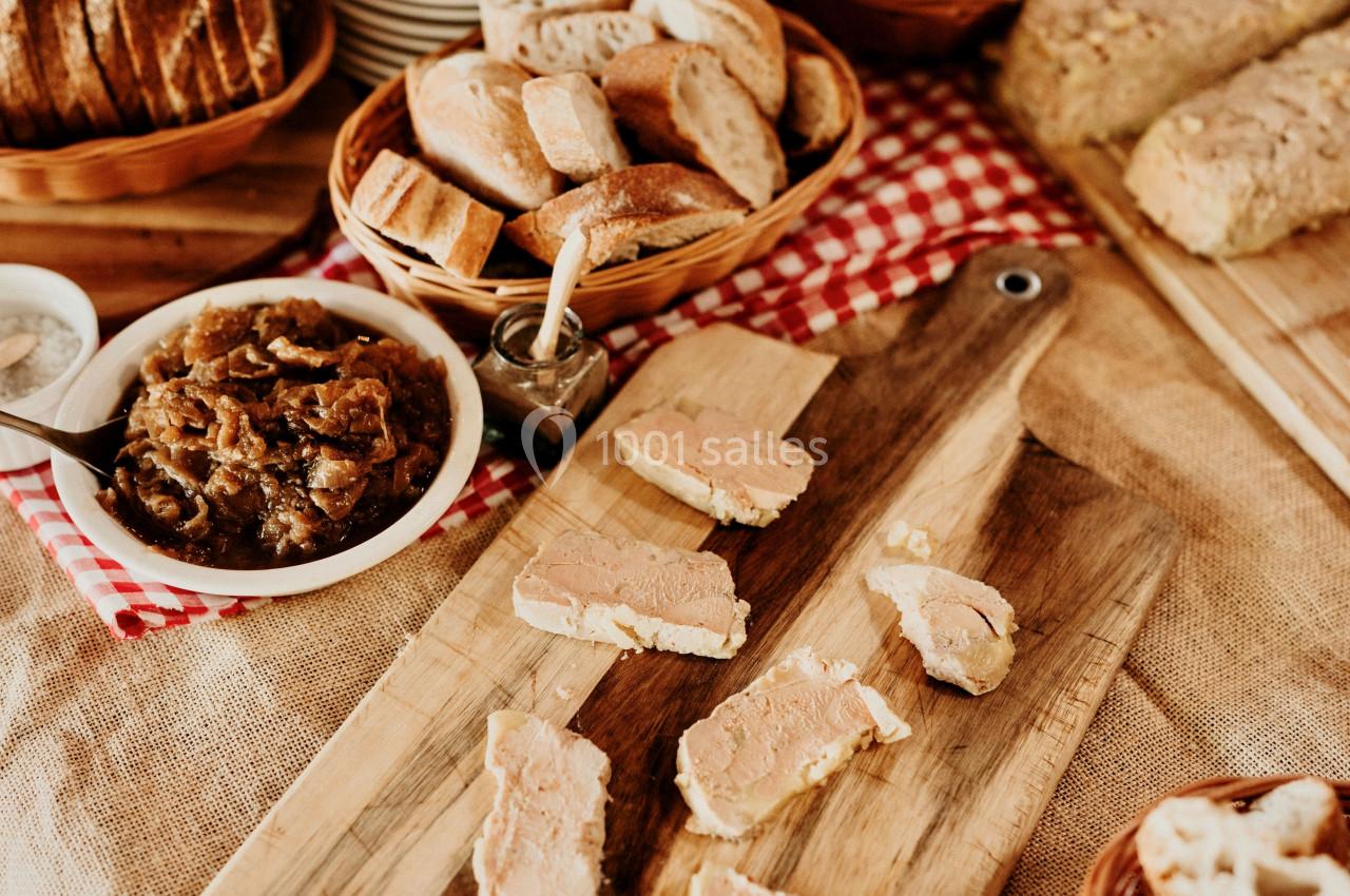 Tranches de foie gras disposées sur une planche en bois, entourées de pain et d'un bol de confit d'oignons.